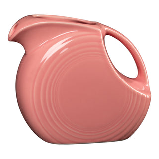 A Fiesta Retired 67 OZ Large Disk Pitcher in peony features a rounded body, large handle, small spout, and subtle concentric circle patterns on lead-safe china. The pitcher is set against a white background.
