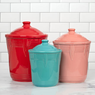 Three Fiesta Retired 2 Quart Medium Chevron Canisters with lids in red, teal, and light pink sit on a white marble countertop, offering stylish airtight storage. A white subway tile backsplash enhances the modern kitchen look.